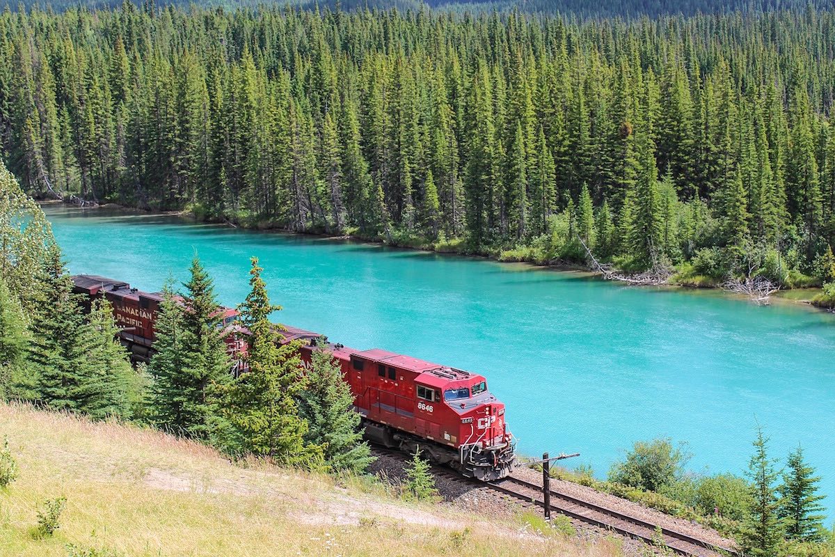 Train passing a bright lake in Alberta in the summer